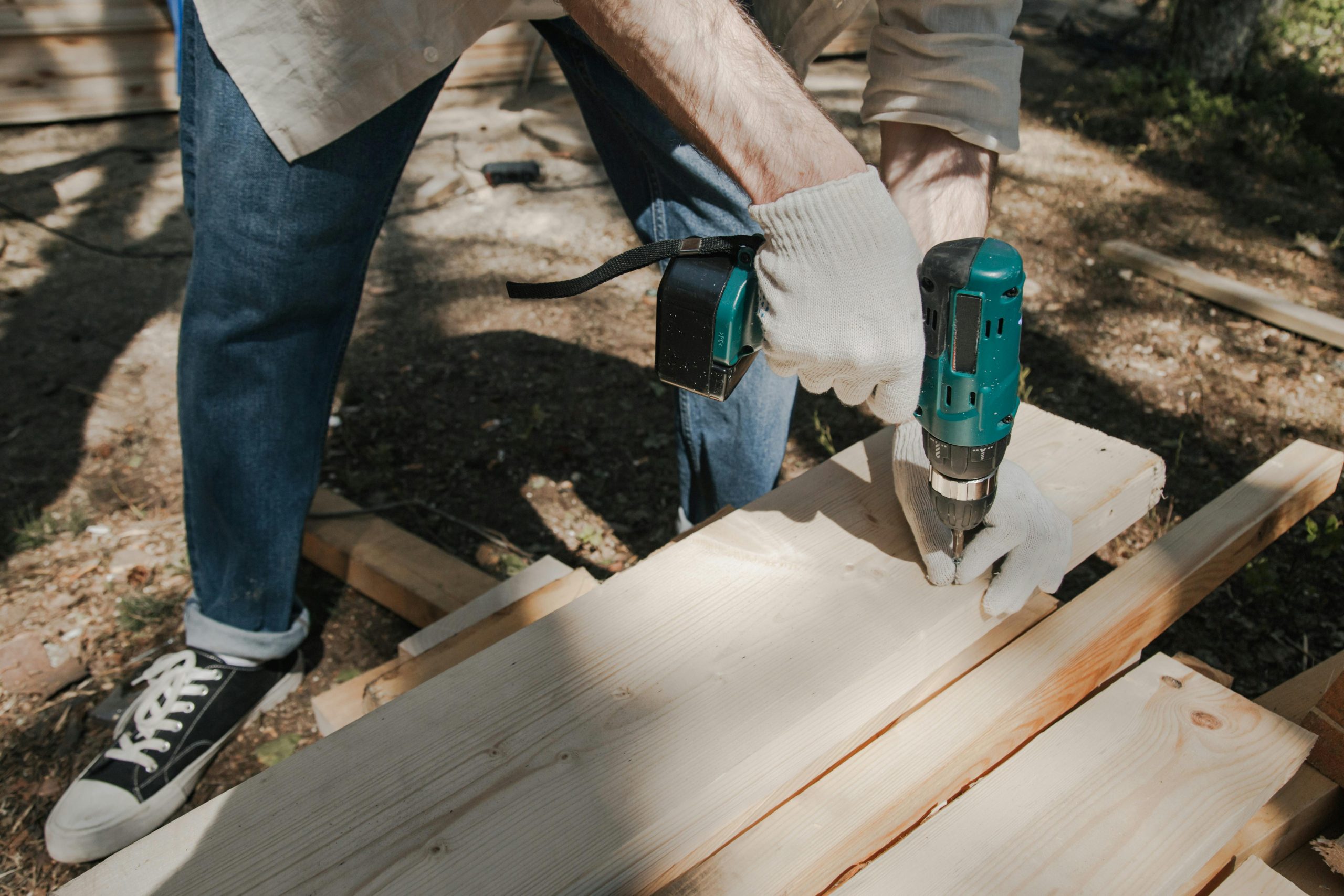 A carpenter using a power tool to drill into wood, showcasing skilled woodworking outdoors.